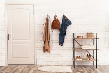 Stylish hallway interior with door, comfortable furniture and clothes on brick wall - obrazy, fototapety, plakaty