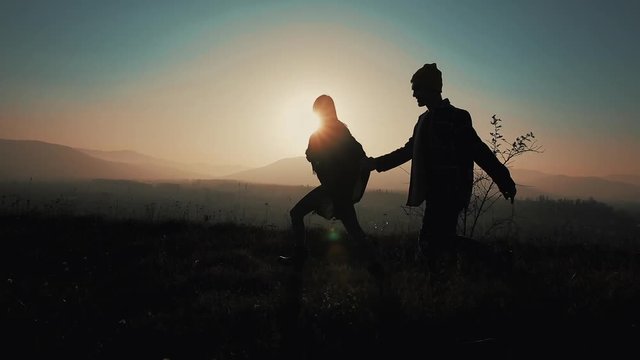 Silhouette of a couple in love in mountains. Hikers man and woman trekking running map at sunset in mountains. They holding hands