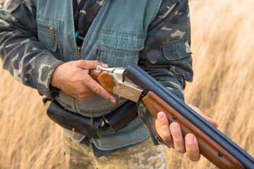 Hunter with a hat and a gun in search of prey in the steppe, reloads the weapon, the smoke from the...