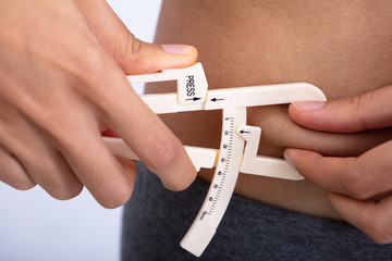 Woman Using Fat Caliper To Measure Body Fat
