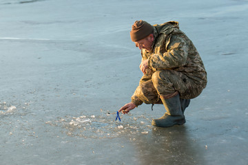 The guy on the winter fishing at the hole catches a small fishing pole. Fishing on the lake with reeds on a beautiful winter day.