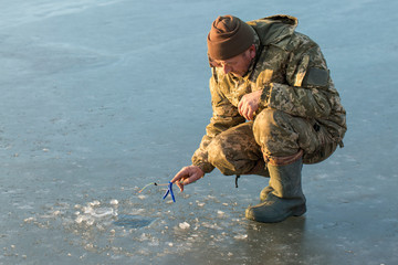 Naklejka premium The guy on the winter fishing at the hole catches a small fishing pole. Fishing on the lake with reeds on a beautiful winter day.