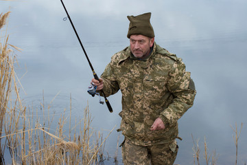Fishing in the reeds for spinning on quiet water. A man in camouflage clothes in cool weather is...