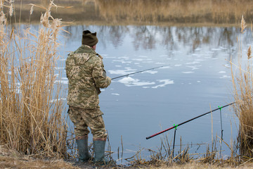 Fishing in the reeds for spinning on quiet water. A man in camouflage clothes in cool weather is fishing on the river bank.