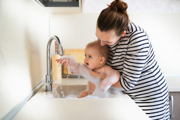 funny baby 6 months bathing in sink in kitchen.Mom