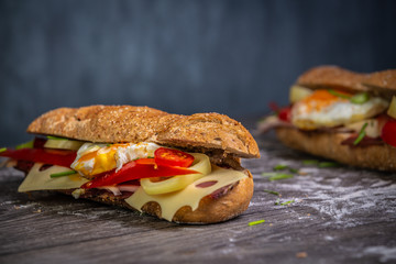 Fresh baguette sandwiches with bacon, cheese, tomatoes on wooden background