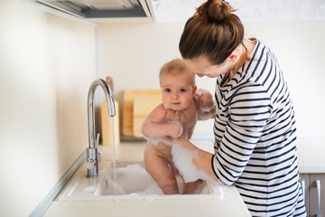 Mom takes care of baby, bathes baby sink with foam