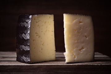 blocks of spanish sheep cheese on wooden board on dark background