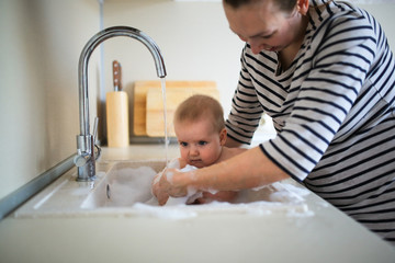 funny baby 6 months bathing in sink in kitchen.Mom