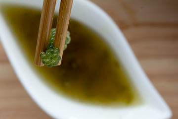 Sea grapes or green caviar and spicy sauce on a white dish the wooden dish made of Japanese style bamboo