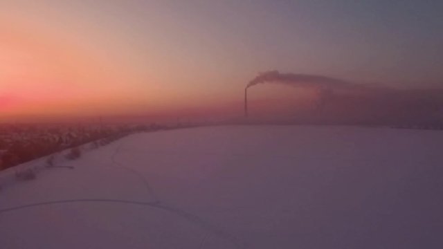 Flying over snow field sunset and lonely chimney-stalk with smoke on the horizon