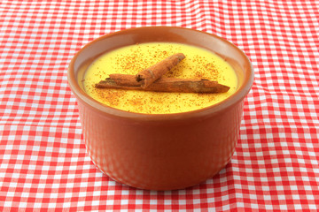 curau, cream of sweet corn and dessert typical of the Brazilian cuisine, with cinnamon placed in a ceramic bowl on a checkered tablecloth.