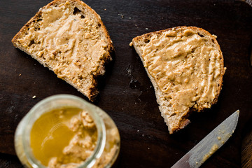 Jar of Creamy Peanut Butter with Bread and Knife on Wooden Surface.
