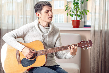 Young attractive musician sitting on a chair playing acoustic guitar. Concept of music as a hobby