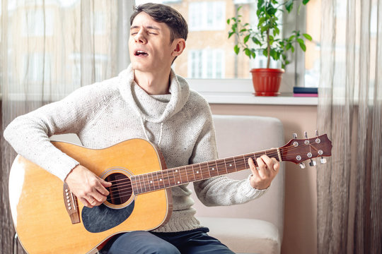 Young attractive musician sitting on a chair playing acoustic guitar. Concept of music as a hobby
