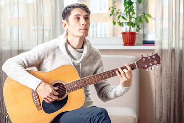 Young attractive musician sitting on a chair playing acoustic guitar. Concept of music as a hobby