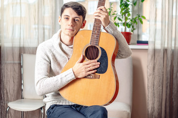 Young attractive male musician sitting on a chair holding an acoustic guitar. Concept of music as a hobby