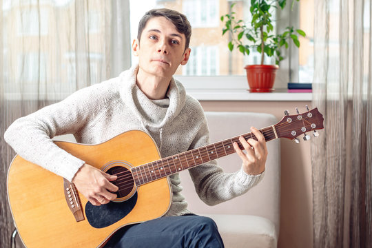 Young attractive musician sitting on a chair playing acoustic guitar. Concept of music as a hobby