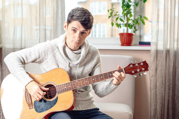 Obraz premium Young attractive male musician sitting on a chair playing acoustic guitar. Concept of music as a hobby