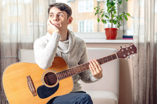 Young attractive male musician sitting on a chair holding an acoustic guitar. Concept of music as a hobby