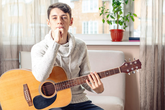 Young attractive male musician sitting on a chair holding an acoustic guitar. Concept of music as a hobby