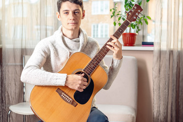 Young attractive male musician sitting on a chair playing acoustic guitar. Concept of music as a hobby