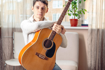 Young attractive male musician sitting on a chair holding an acoustic guitar. Concept of music as a hobby