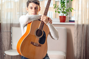 Young attractive male musician sitting on a chair holding an acoustic guitar. Concept of music as a hobby