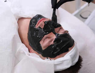 Spa therapy for men receiving facial black mask.