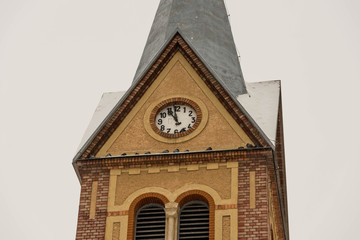 Clock on focus on catholic church on a cloudy , snowy winter day.
