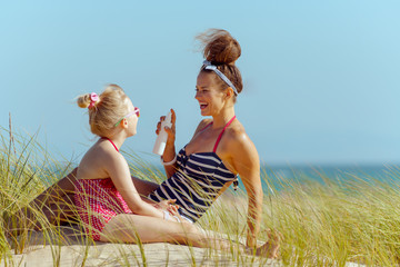 smiling mother and child on ocean coast applying sun screen