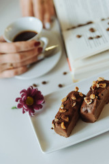 Chocolate pastries and the cup of coffee in the hands near the book on the white background.