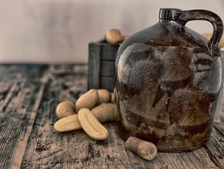 vintage moonshine jug on a rustic wooden table with potatoes and corn cob cork