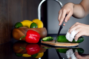 Young loser man male cutting vegetables: cucumber, pepper on wooden desk in kitchen with wounded injured fingers. Trying to make breakfast, lunch or dinner. Bachelor in kitchen concept