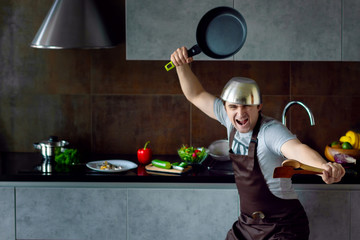 Funny loser man male with metal pan on head frying pan and wooden kitchen utensils in pose of ninja...