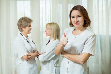 Fototapeta premium beautiful woman doctor in white coat at the age of standing against the background of his colleagues with a gesture of the hand