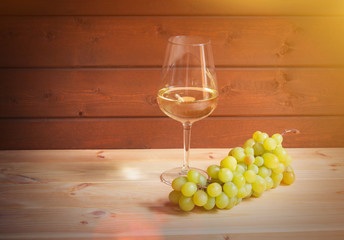 Glass of white wine and green grape branch on wooden table. View with copy space.