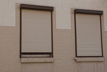 two windows closed by roller shutters on a brown wall