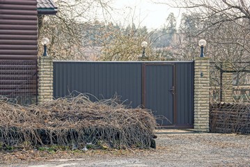 closed gray metal gates and a fence on the street overgrown with dry vegetation