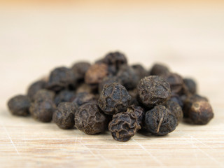 A pile of black pepper grains on a wooden plank.