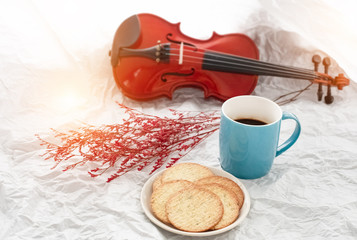 The ceramic coffee cup put beside dish of biscuit,in front of blurred violin,blurry light design background