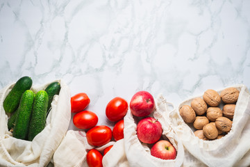 Fresh cucumbers, tomatoes, apples, and walnuts in reusable cotton bags, top view