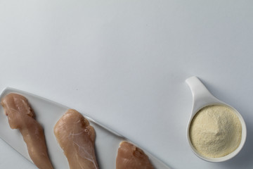 Raw chicken breasts and a scoop whey protein powder on a white table.Top view. Space Text. Sport nutrition