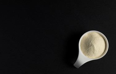 Whey protein powder sports bodybuilding supplement. Top view white porcelain scoop with vanilla flavor powder. Black background and copy space