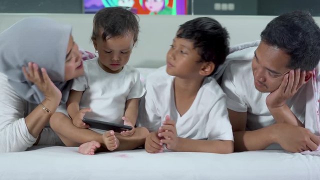 Happy Asian family lying on the bed while the mother and son kissing the little girl. Shot in 4k resolution at home