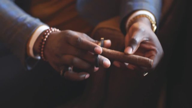Closeup of African american manly hands cutting precious cigar.