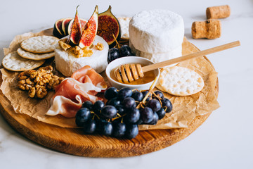 Camembert cheese, figs, jamon, honey and grapes. Cheese plate on marble background