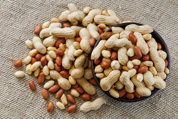 Peanuts in the shell and peeled close-up in cups. Roasted peanuts in their shells and peeled against a brown cloth.