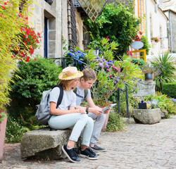 Teenagers travel concept. Children with map sitting on the bench in the street of an old town,...