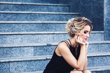 Fototapeta na wymiar gorgeous elegant woman in a black dress sits on the steps and waits thoughtfully.